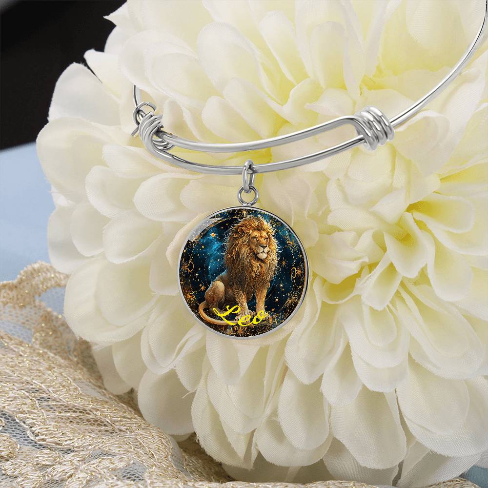 A silver bracelet on a white flower with a round charm featuring an illustrated lion against a starry night background and the word "Leo" in yellow, enhanced by an 18k gold finish, showcasing the elegance of personalized jewelry. This is the Leo Zodiac Bangle Bracelet With Optional Personalization by ShineOn Fulfillment.